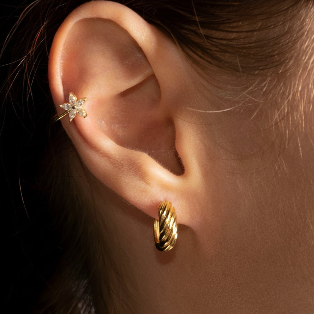 Close-up of an ear wearing a gold earring with a blurred background