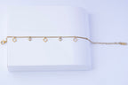 A delicate stainless steel chain bracelet with three small open diamond-shaped charms and two small round bezel-set clear stones horizontally on a white book-like prop against a light background.