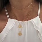 Close-up of a person wearing two gold necklaces with pendant details on a white top.