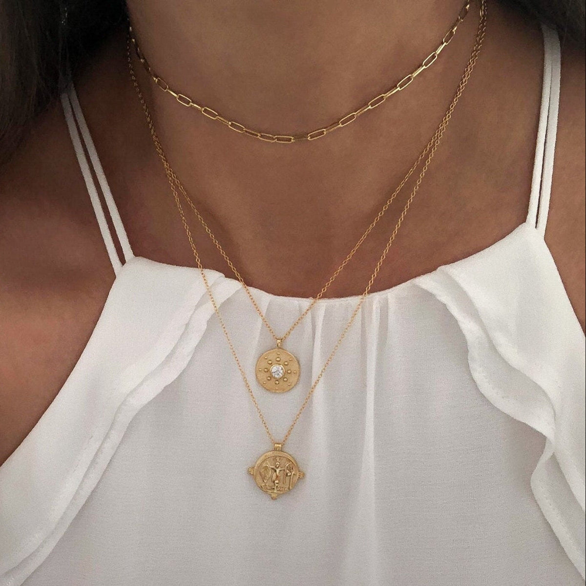 Close-up of a person wearing two gold necklaces with pendant details on a white top.