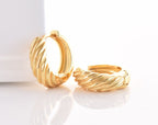 A pair of gold-colored twisted croissant hoop earrings on a white background.